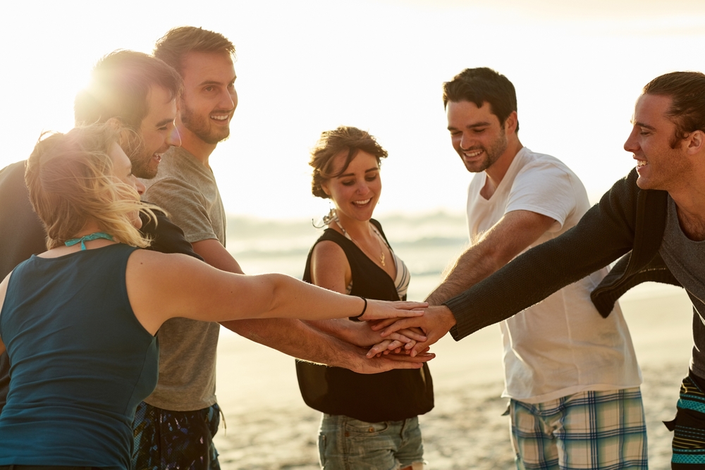 a group of coworkers join hands for a team cheer before a team building activity on the beach
