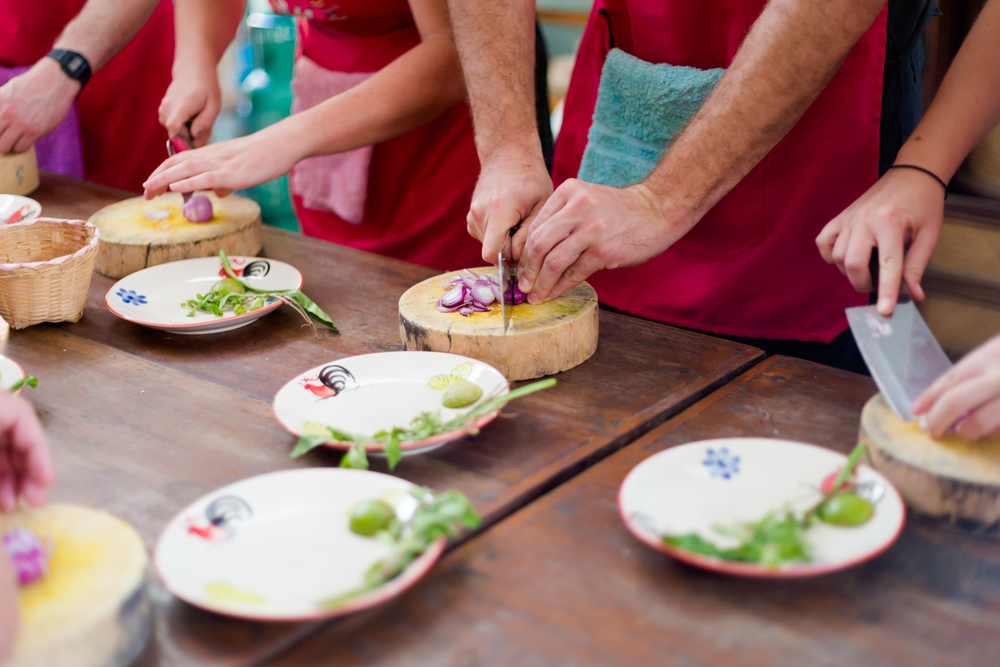 a group of coworkers try their hands at cooking Thai food in a class while on a corporate retreat